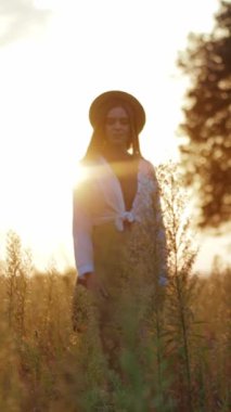 Şık şapkalı bir kadın, gün batımında sıcak bir parıltı yayarken açık bir alanda zarif bir şekilde duruyor. Arabası yakınlarda, ileride bir macera olduğunu gösteriyor.