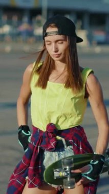 Genç bir kadın bir kaykay tutuyor, paten ve şehir keşfi tutkusunu sergiliyor, kendini ifade etme ve özgürlüğünü somutlaştırıyor