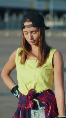 Şapka ve ekose gömlekli kendine güvenen genç bir kadın kaykay tutkusu sergiliyor, sörf tahtasını dinamik pozlarda tutuyor, enerji saçıyor.