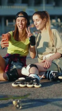 İki genç kadın açık havada güneşli bir günün tadını çıkarıyorlar, yerde oturup telefonlarını kontrol ediyorlar. Neşeli bir selfie çekerken ruhları parlıyor.