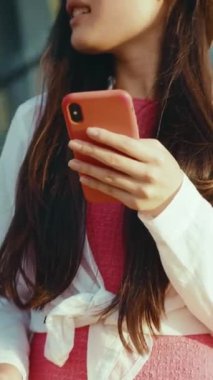 Genç bir kadın, neşeli bir şekilde akıllı telefonunu tutuyor. Çevresi canlı ve canlı bir geçmişle çevrili.