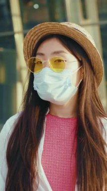 Şık bir kadın, bir yüz maskesi, şık bir güneş gözlüğü ve şık bir şapka ile süslenmiş, şehir ortamında geziniyor.