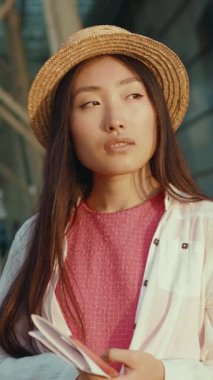 Şık bir hasır şapka giyen, elinde bir defter tutan ve kendine güveni olan şık bir genç kadın.