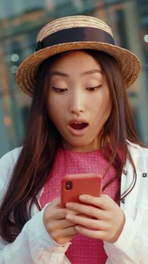 Şık bir genç kadın akıllı telefonuyla derinden meşguldür. Çevresi canlı, modern bir şehir zeminiyle çevrilidir.