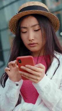 Modayı takip eden genç bir kadın açık havada akıllı telefonuyla mutlu mesut meşgul, modern bir yaşam tarzı sergiliyor.