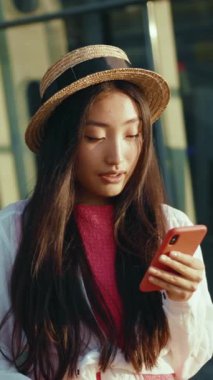 Moda bir genç kadın akıllı telefonuyla açık hava ortamında, modaya uygun bir görünüm sergiliyor..