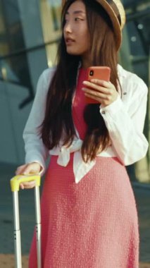 Şık pembe bir elbise giyen şık bir kadın akıllı telefonunu dikkatle kontrol ediyor ve inkar edilemez bir moda yaratıyor.