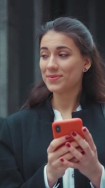 Genç bir kadın bugün canlı bir şehir ortamında akıllı telefonuyla konuşurken neşeli bir şekilde gülümsüyor.