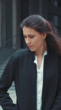 Tarz sahibi siyah ceketli ve beyaz bluzlu genç bir kadın açık havada duruyor, özgüven ve zarafet saçıyor.