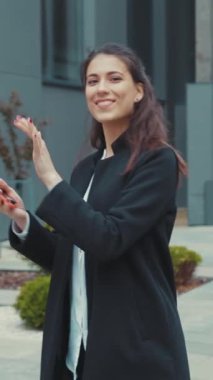 Siyah ceketli kendine güvenen genç bir kadın açık havada jest yapar, profesyonelliği ve yaklaşımı somutlaştırır..