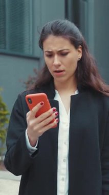 Genç bir kadın dışarıda duruyor, akıllı telefonuna dalmış, konsantrasyonu ve modern bağlantıyı yansıtıyor..