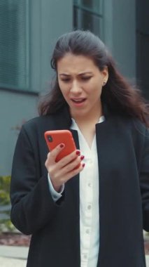 Yoğun bir şehir ortamında akıllı telefonunu kontrol eden genç bir kadın endişeli ve endişeli görünüyor.