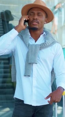 Beyaz gömlekli ve şapkalı şık bir genç modern şehir ortamında önemli bir telefon görüşmesi yapıyor.