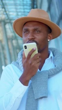 Moda şapkalı şık ve şık bir adam dışarıda akıllı telefonunu kullanırken sohbet ediyor.