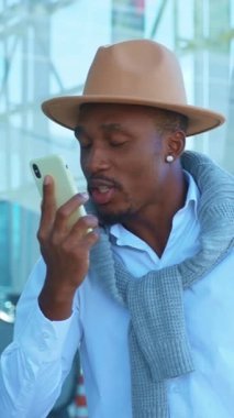 Son moda şapkalı çok şık bir adam modern bir arka plana karşı akıllı telefonuyla sohbet ediyor.