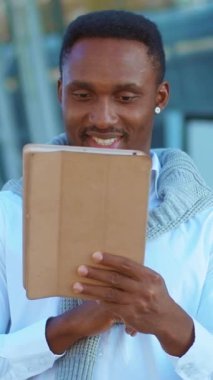 Açık havada rahatça tablet okuyan bir adam modern teknolojinin canlı bir ortamda bütünleştiğini gösteriyor.