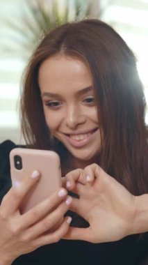 Genç bir kadın, rahat bir ortamda doğal ışıkla çevrili akıllı telefonunu kullanırken güvenli bir şekilde ışıldıyor.