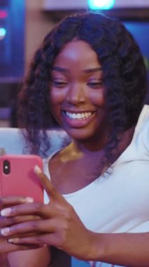 Genç bir kadın akıllı telefonuyla canlı renklerle dolu şık ve modern bir ortamda etkileşime girer.