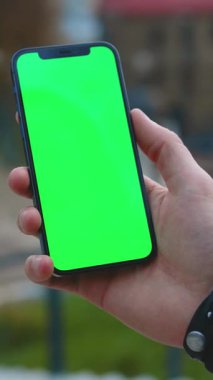 Bir kişi, uygulamalar ve reklamlar için ideal, parlak yeşil ekranlı, modern bir akıllı telefon tutuyor.