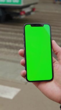 Parlak, canlı yeşil bir ekran gösteren akıllı telefonu sıkıca kavrayan bir el. Örtüler ve tasarımlar için mükemmel.