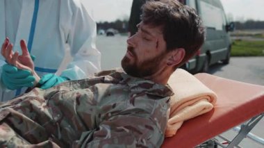 Dışarıdaki sıhhiyeci cesedi inceliyor ve ambulansın yanındaki tekerlekli sandalyede acı çeken askerlere ilk yardım sağlıyor. Askeri bir kavram. - Savaş. Açık havada.