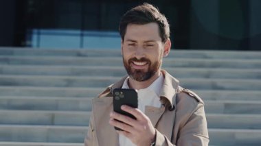 Yakından bakınca, ceketli, sakallı çekici bir adam güneş ışığında gölün kenarında akıllı telefon standı kullanıyor. Yavaş çekim