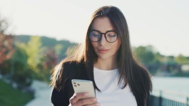 Şehir merkezinde gün ışığında telefonla gezen genç ve çekici bir kadın göl kenarındaki parka bakıyor. Cep telefonu olan bir portre kızı. Yavaş çekim