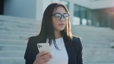 Şehir merkezinde güneş ışığında telefonu kullanan gözlüklü çekici bir kadın göl kenarındaki parka bakıyor. Cep telefonu olan bir portre kızı. Yavaş çekim