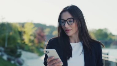 Şehir merkezinde gün ışığında telefonla yürüyen çekici genç bir kadın göl kenarındaki parka bakıyor. Cep telefonu olan bir portre kızı. Yavaş çekim
