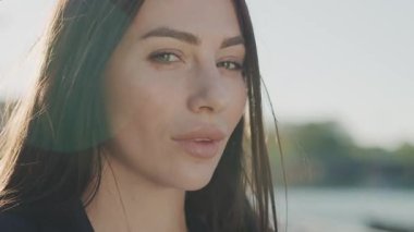 Gün batımında genç ve çekici bir kadının portresi kameraya gülümsüyor. Rüzgârlı. Dışarıda dur ve rahatla. Kapatın. Yavaş çekim