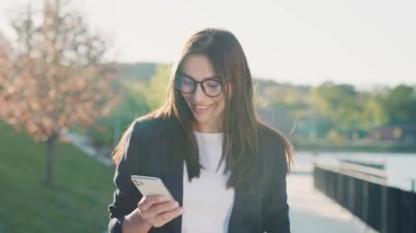 Şehir merkezinde gün ışığında telefonla yürüyen çekici bir kadın göl kenarındaki parka bakıyor. Cep telefonu olan bir portre kızı. Yavaş çekim