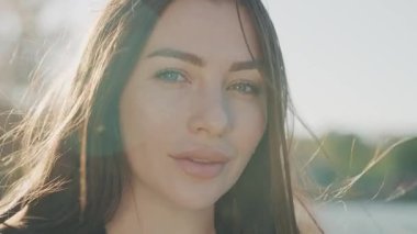 Gün batımında kameraya gülümseyen çekici bir kadınla yüzleş. Rüzgârlı. Dışarıda dur ve rahatla. Yavaş çekim