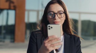 Gün ışığında genç ve çekici bir kadın şehir merkezinde telefonla gülümsüyor ve mutlu oluyor. Cep telefonu olan bir portre kızı. Yavaş çekim