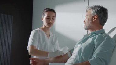 Modern bir klinikte, ışık odasındaki hastadan kan almaya hazırlanan bir doktor. Kan bağışı. Kadın hemşire ve sabırlı adam oturmuş gülümsüyor. Yavaş çekim