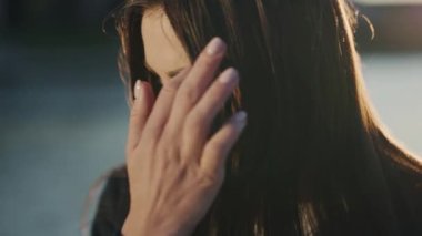 Şehir merkezindeki kameraya gün ışığında bakan çekici genç bir kadını kapatın. Açık hava portresi kızı. Rüzgârlı. Yavaş çekim