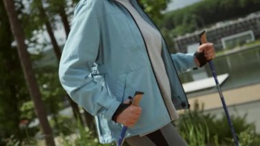 Gri saçlı, zarif yaşlı kadın ormanda İskandinav yürüyüşü yapıyor. Yürüme konsepti. Ahşap içinde güzel görünümlü beyaz bir kadın. Yaz zamanı. Spor, eğlence, spor, spor. Sağlıklı bir yaşam tarzı. Açık hava.