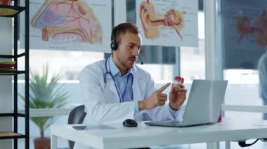 Kulaklıklı, beyaz önlüklü, çekici genç bir doktor görüntülü sohbette laptoptan danışmanlık mesafesindeki hastayı kullanıyor. Röntgeni durdurun. Yavaş çekim
