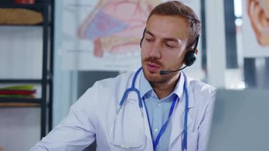 Kulaklıklı beyaz ceketli yüz doktoru dizüstü bilgisayarla konferans görüşmesi yapıyor. Video sohbetinde hastaya danışmanlık yapıyorum. Röntgene bak. Yavaş çekim