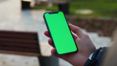 NEW YORK - 19 Aralık 2020: Kapalı eller açık havada dikey yeşil ekran standı olan telefonu kullanın. Cep telefonu iletişimi dokunmatik ekran dinleme medyası. Yavaş çekim