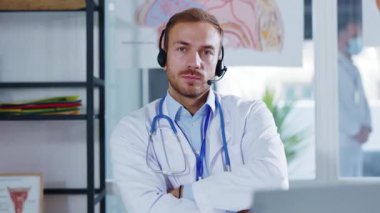 Ofiste kulaklıkları olan genç ve ciddi bir doktor kameraya çevrimiçi danışmanlık yapıyor. Hastanedeki terapi videosu tıbbı arıyor. Yavaş çekim
