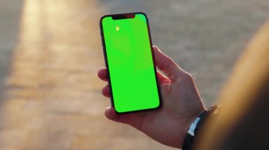 NEW YORK - 19 Aralık 2020: Kentteki dikey yeşil ekran arka plan güneş ışığı yolu ile dokunmatik telefon kullanan genç adamı kapatın. İnternet krom açık hava cep telefonu akıllı telefonları kayıyor. Yavaş çekim