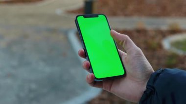 NEW YORK - 19 Aralık 2020: Kentteki dikey yeşil ekran arka plan aydınlatma yolu ile dokunmatik telefon kullanan boş bir sokak adamı eli üzerinde bulanıklaştı. İnternet krom açık hava cep telefonu akıllı telefonları kayıyor. Yavaş çekim