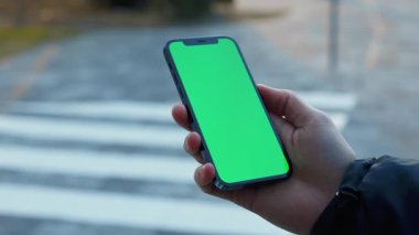 NEW YORK - 19 Aralık 2020: Elle çekilen adam güneşli cadde üzerinde dikey yeşil arka plan yaya geçidi olan telefonu kullanıyor. Cep telefonu iletişimi dokunmatik ekran dinleme medyası. Yavaş çekim