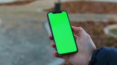 NEW YORK - 19 Aralık 2020: Şehrin arka planında dikey yeşil ekran güneş ışığı yolu ile dokunmatik telefon kullanan açık hava adamı eli bulanıklaştı. İnternet krom açık hava cep telefonu akıllı telefonları kayıyor. Yavaş çekim