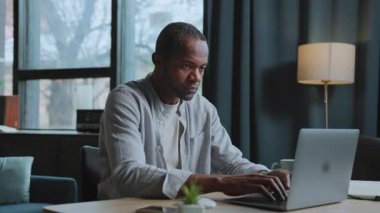 Sıradan tişörtlü, dizüstü bilgisayarda oturup klavyede yazan odaklanmış Afro-Amerikan bir adam görüntüsü. Çatı katında serbest çalışan bir işçi. Kapalı