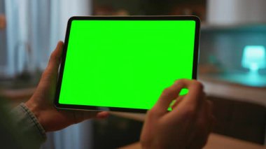 Mans dijital tableti yeşil ekranlı, kromakey modern mutfağın bulanık arka planında tutuyor. Evde alet kullanan bir adam. Yatay konum