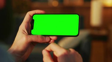 Erkek ellerinin akıllı telefonu yatay pozisyonda tutarken, ekranda yazarken ve apartmanın bulanık arka planında izlemek için film seçerken yatay çekim. Kapalı
