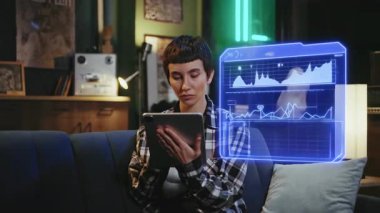 Konforlu bir oturma odasında, genç bir çift kanepede dinleniyor, her biri tabletlerinde özümsenmiş, ortak bir alandaki modern bağlantıyı vurguluyor.