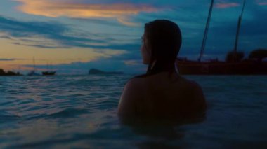 Sakin bir video günbatımında okyanusta zarif bir şekilde yüzen bir kadını gösteriyor, ılık renkler suya yansıyor, sükunet yaratıyor.