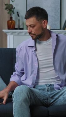 Bir adam kendini tamamen düşüncelerine dalmış, rahat bir şekilde otururken yeşil bir kitap okumaya kaptırmış.